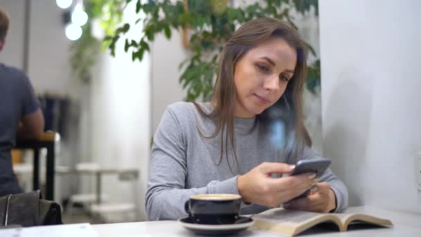 Güzel kadın bir kafede vaktini harcıyor: smartphone kullanarak ve kahve içme — Stok video