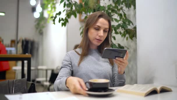 Bella donna trascorre il suo tempo in un caffè: rmakes foto per i social network - caffè e libro — Video Stock
