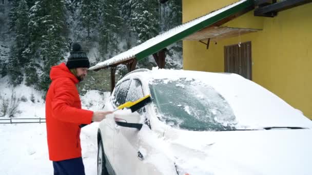 El hombre limpia el coche de la nieve cerca de su casa — Vídeos de Stock