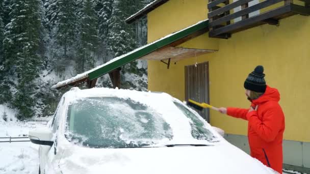 Мужчина убирает машину со снега возле своего дома — стоковое видео
