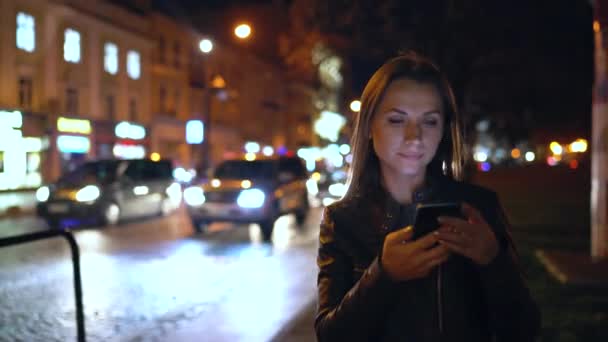 Ελκυστική γυναίκα χρησιμοποιώντας ένα smartphone, ενώ το περπάτημα στους δρόμους της πόλης το βράδυ — Αρχείο Βίντεο
