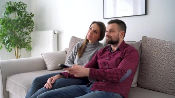Un par de amantes ven la televisión abrazada en el sofá de la nueva casa y ven una película juntos. Concepto de: ocio, relax, tv . — Vídeos de Stock