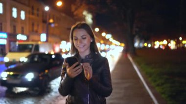 Akşam şehrin sokaklarında yürürken bir akıllı telefon kullanan çekici kadın