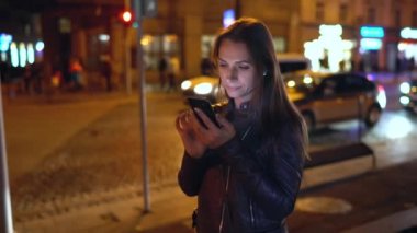 Akşam şehrin sokaklarında yürürken bir akıllı telefon kullanan çekici kadın