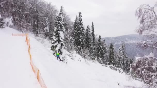 Vista aérea de snowboarder extremo montando nieve fresca en polvo por la empinada ladera de la montaña y salta sobre la valla de la pista de esquí — Vídeo de stock