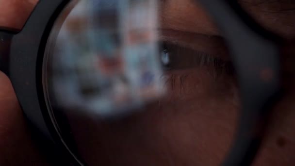 Man in glasses looking on the monitor and surfing Internet. The monitor screen is reflected in the glasses — Stock Video