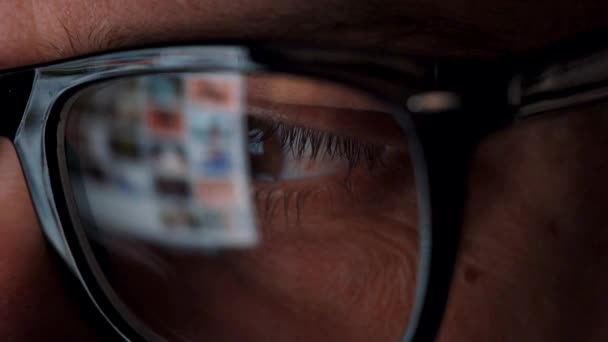 Hombre con gafas mirando en el monitor y navegando por Internet. La pantalla del monitor se refleja en las gafas — Vídeo de stock