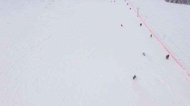 Лижник і сноубордист спуститися на схилі гори з кольоровим димом в своїх руках, серед інших людей на гірськолижний курорт в Україні. Пташиного польоту — стокове відео