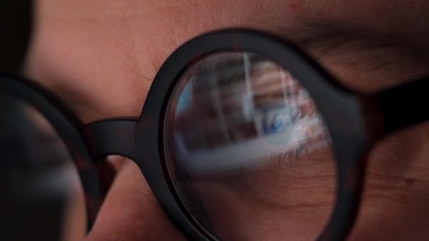 Man in glasses looking on the monitor and surfing Internet. The monitor screen is reflected in the glasses — Stock Video