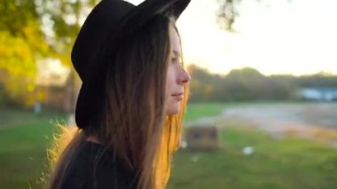 Siyah şapkalı güzel gülümseyen kız açık havada yürüyüş arka planda bir gün batımı ile