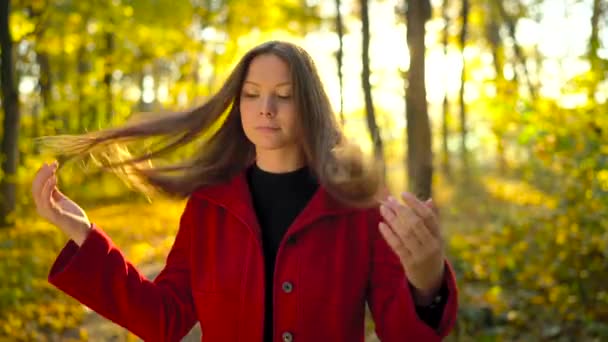 Porträtt av en vacker fundersam tjej i röd jacka med en gul lönnlöv i bakgrunden i skogen höst — Stockvideo