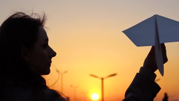 Kobieta rozpoczyna papierowy samolot na tle zachodu słońca. Koncepcja chce pojechać na wakacje lub podróży. Zwolnionym tempie — Wideo stockowe