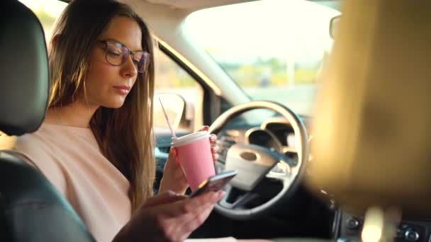 Vrouw in glazen spreekt op de smartphone en drinkt koffie in de auto — Stockvideo