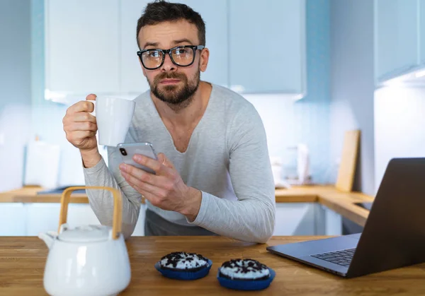 Pria berjenggot sarapan di dapur dan menggunakan smartphone — Stok Foto