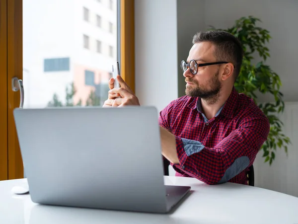 Homme dans des lunettes assis au bureau à la maison et travaillant sur un ordinateur portable un — Photo