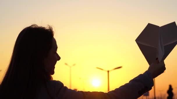 Femme lance l'avion en papier sur fond de coucher de soleil. Concept de vouloir partir en vacances ou en voyage. Mouvement lent — Video