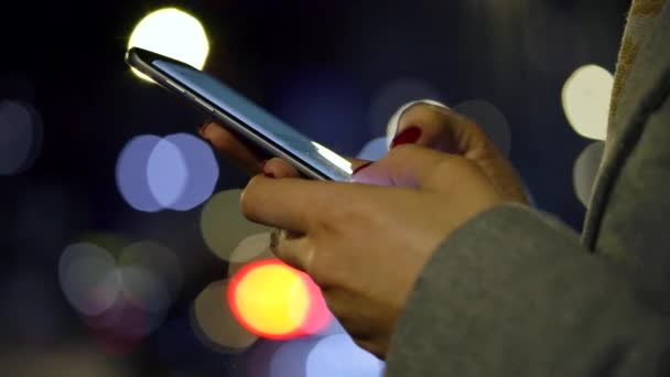 Manos femeninas usando smartphone sobre fondo borroso de luces de ciudad — Vídeos de Stock