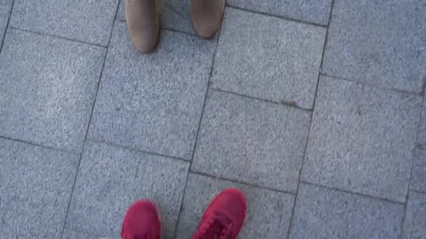 Κάτοψη του αρσενικό πόδια σε πάνινα παπούτσια, η οποία πάει κατά μήκος του πεζοδρομίου, πληρούν γυναικεία πόδια σε μπότες, και στη συνέχεια να περπατήσει μαζί — Αρχείο Βίντεο