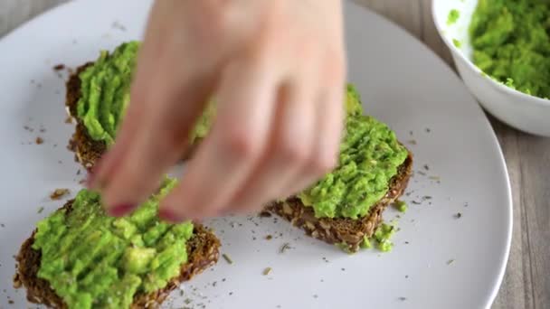 Stendere il purè di avocado sul pane tostato e cospargere di sale e spezie. Colazione vegana sana . — Video Stock