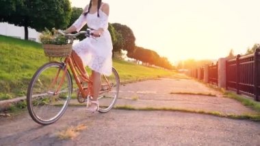 Genç güzel kadın günbatımında bir bisiklet sürme. Ağır çekim