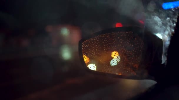 Городские огни видны на автомобиле зеркало заднего вида ночью во время дождя — стоковое видео