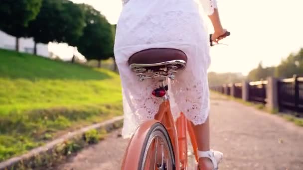 Mulher bonita nova que monta uma bicicleta no por do sol - visão traseira — Vídeo de Stock
