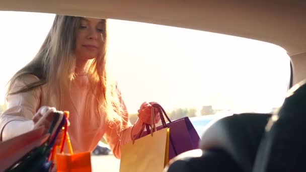 Hermosa chica pone bolsas de compras en el maletero de un coche y se va, con la intención de alejarse en coche. Movimiento lento . — Vídeo de stock