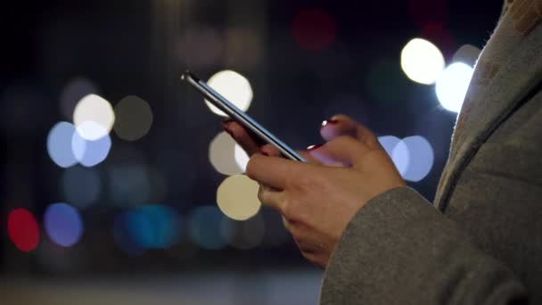 Manos femeninas usando smartphone sobre fondo borroso de luces de ciudad — Vídeo de stock