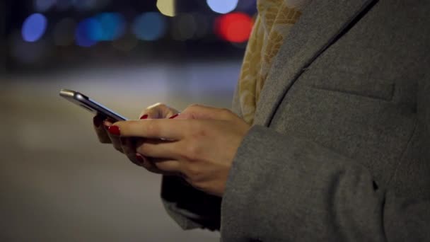 Mãos femininas usando smartphone no fundo de luzes turvas da cidade — Vídeo de Stock