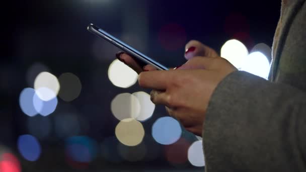 Manos femeninas usando smartphone sobre fondo borroso de luces de ciudad — Vídeo de stock