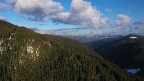 Pohled ze vzduchu na mraky na modré obloze přes úžasnou krajinu vysokých zasněžených hor a jehličnaté lesy na svazích — Stock video