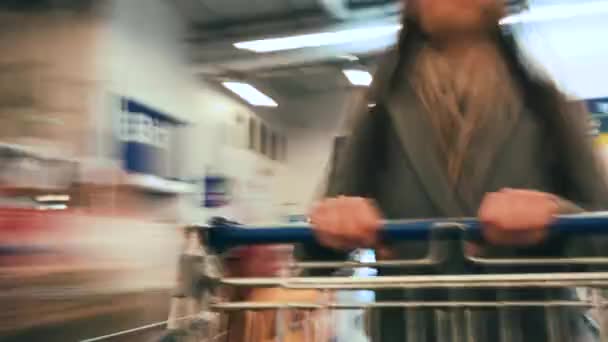 Caducidad del carro de la compra moviéndose entre varios pasillos y sección en el gran supermercado. Mujer de compras en una tienda de comestibles — Vídeo de stock