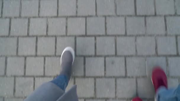 Вид зверху на чоловічі та жіночі ноги, що йдуть уздовж тротуару. Жінка п'є каву — стокове відео