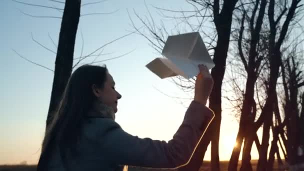 Женщина бежит и запускает бумажный самолет на фоне заката. Концепция желания поехать в отпуск или путешествовать. Медленное движение — стоковое видео