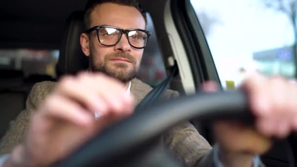Удовлетворенный бородатый мужчина в очках водит машину по улице в солнечную погоду — стоковое видео