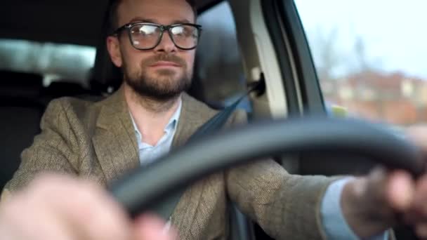 Задоволений бородатий чоловік в окулярах водить машину по вулиці в сонячну погоду — стокове відео