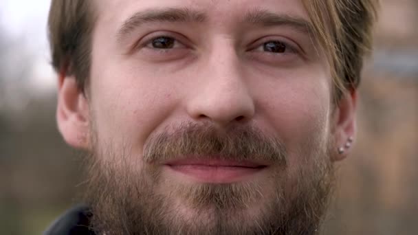 Fiatal szakállas ember néz a kamerába, és mosolyog — Stock videók