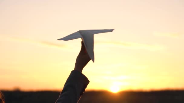 Kvinna lanserar pappersflygplan mot solnedgången bakgrund. Begreppet vilja åka på semester eller resor. Slow motion — Stockvideo