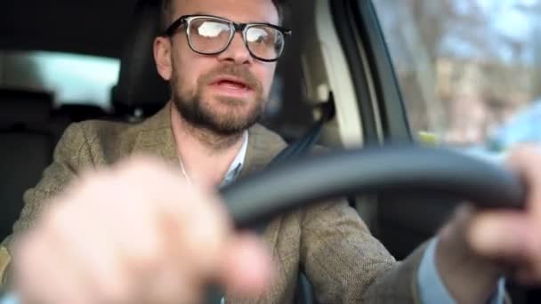 Бородач в очках водит машину и кричит на кого-то рядом с ним или снаружи — стоковое видео