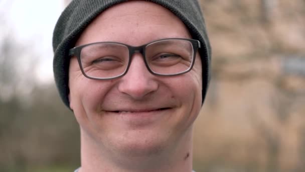 Joven con gafas y un sombrero y mirando a la cámara y sonriendo — Vídeo de stock