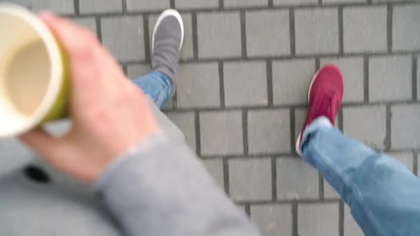 Von oben auf männliche und weibliche Beine, die auf dem Bürgersteig spazieren. Frau trinkt Kaffee — Stockvideo