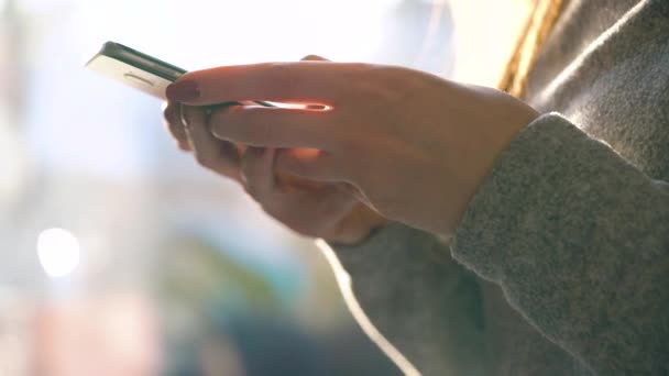 Manos femeninas usando smartphone contra un paisaje urbano borroso al atardecer — Vídeos de Stock