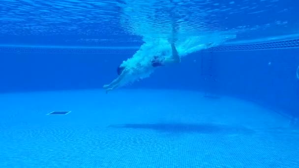 Disparos bajo el agua mientras un hombre se sumerge en la piscina y nada bajo el agua — Vídeo de stock