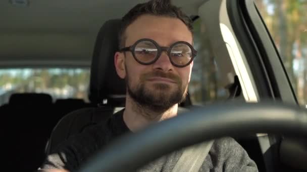 Uomo barbuto soddisfatto con gli occhiali alla guida di una macchina in fondo alla strada con tempo soleggiato — Video Stock