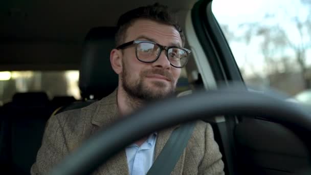 Hombre barbudo satisfecho en gafas que conducen un coche por la calle en tiempo soleado — Vídeos de Stock