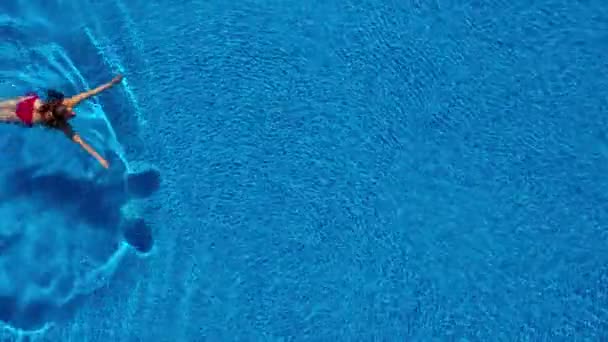 View from the top as a woman in a red swimsuit swims in the pool — Stock Video