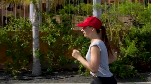 La mujer corre por la calle entre las palmeras. Vida activa saludable. Movimiento lento — Vídeos de Stock