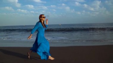 Mavi elbiseli kadın siyah bir volkanik plajda çalışır. Yavaş hareket