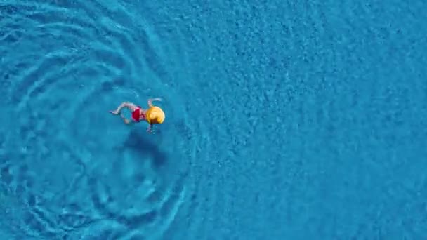 Vista dall'alto come una donna in costume da bagno rosso e un grande cappello giallo nuota in piscina — Video Stock