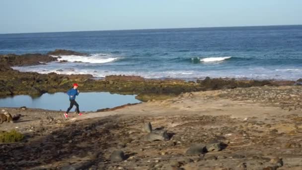 Frau läuft am steinigen Ufer des Ozeans entlang. Gesunder aktiver Lebensstil — Stockvideo